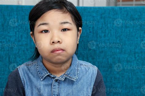 Little Southeast Asian malay girl child sit on blue sofa serous mood ...