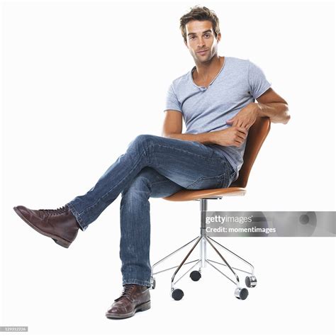 Portrait Of Young Man Sitting On Chair With Legs Crossed Against White ...