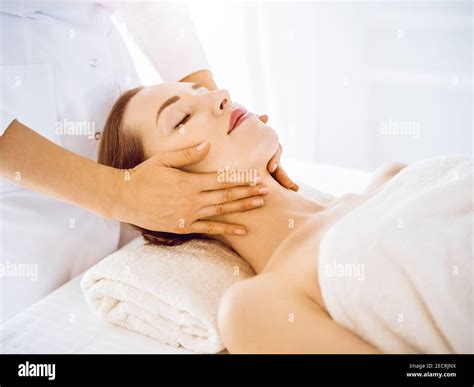 Beautiful woman enjoying facial massage with closed eyes in sunny spa ...