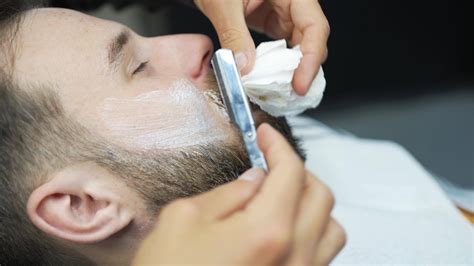 Barber uses straight razor to shave man's neck and face to shape facial ...