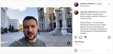 Zelensky wearing a green shirt speaks in a dimly-lit room. An out-of-focus Christmas tree is in the