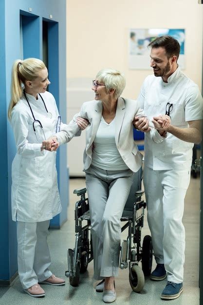 Femme mûre se levant du fauteuil roulant avec l'aide de deux médecins ...