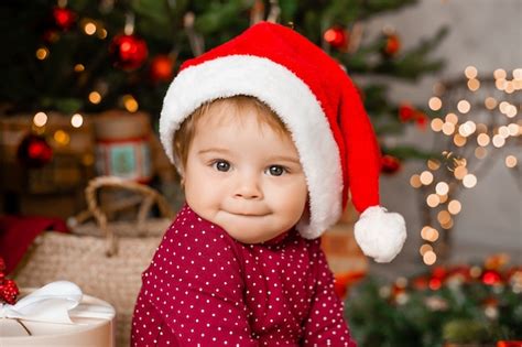 Cute baby santa sits at home near the christmas tree with gifts ...