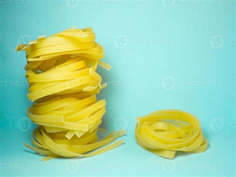 Nests of pasta on a blue background. Culinary background. Pyramid of noodles. Curled pasta on ...