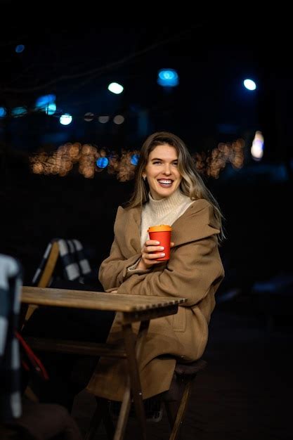 Lonely beautiful girl in the evening at a table in a street cafe with a ...