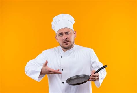 Confiant jeune beau cuisinier en uniforme de chef tenant et pointant ...