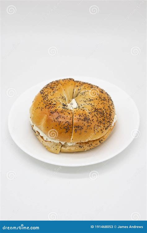 Large Poppy Seed Bagel Filled with Cream Cheese on a White Plate with a ...
