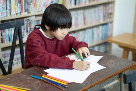 Asian boy writing in notebook, doing homework in a classroom at school ...