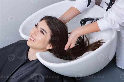 professional hairdresser washing hair of young woman in beauty salon ...