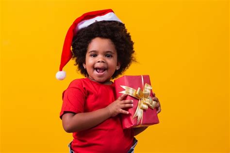 Smiling afro child in santa claus red hat holding christmas gift in ...