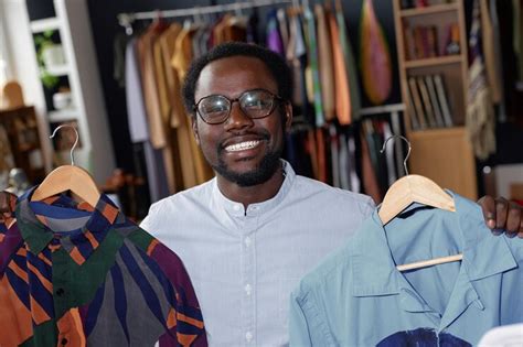 Portrait of smiling black man holding hangers with second hand shirts ...