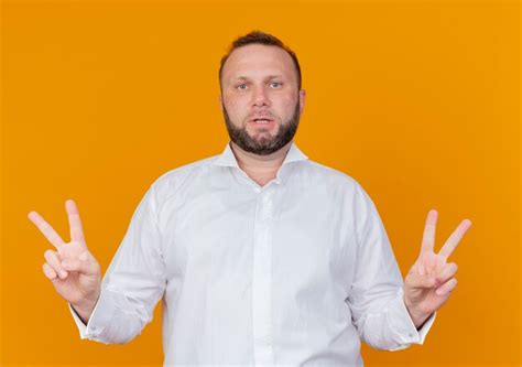 Homme barbu portant une chemise blanche montrant v-sign debout sur un ...