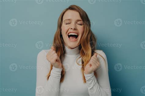 Young woman with closed eyes clenching fists, mouth wide open with cry ...