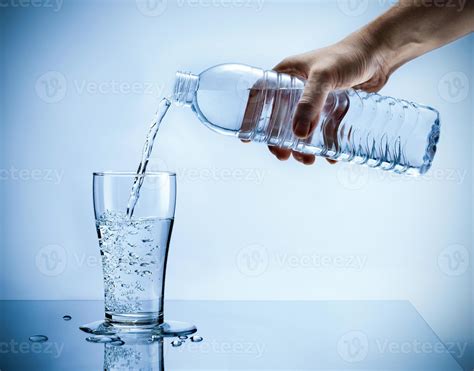 Hand pouring fresh pure water from bottle into a glass on the table ...