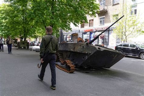 A man walks past a burnt armoured personnel carrier near buildings destroyed in the course of Ukrain