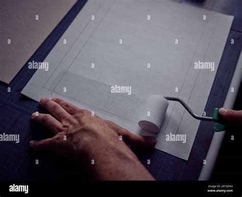 Crop artisan holding roller and plastering sheet of marked paper with ...