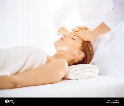 Beautiful woman enjoying facial massage with closed eyes in sunny spa ...