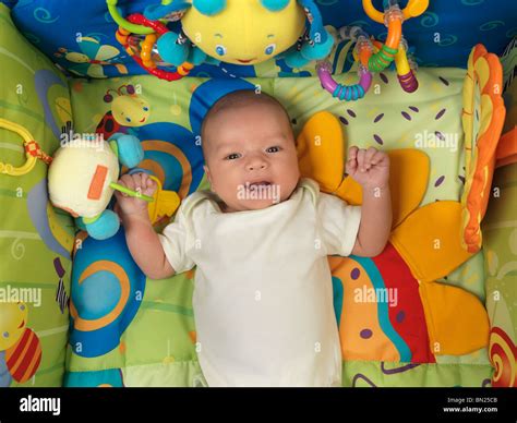 Happy smiling six week old cute baby boy lying in a colorful play mat ...