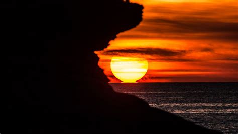 Download wallpaper 1366x768 rock, silhouette, sea, sunset tablet ...