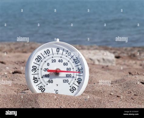 a round thermometer on the hot sand on the beach showing about 90 ...