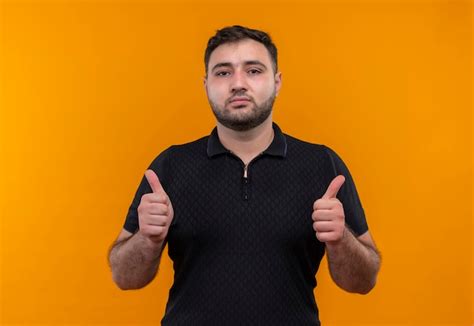 Young bearded man in black shirt looking confident showing thumbs up ...