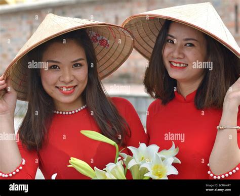 Two young Vietnamese women wear Asian conical hats and red Vietnamese ...