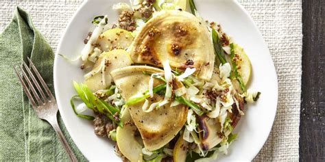 A plate with pierogies sausages and cabbage served with a small bowl of sour cream