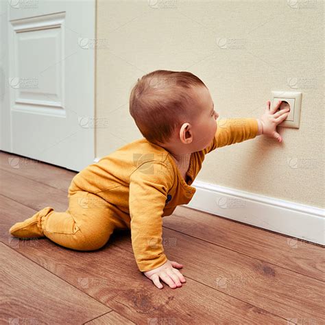 蹒跚学步的婴儿把手伸进家里墙上的插座里。儿童手指触电的危险及保护