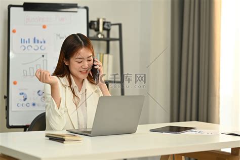 漂亮的女性财务顾问与客户进行电话交谈，并在明亮的办公室使用笔记本电脑高清摄影大图-千库网