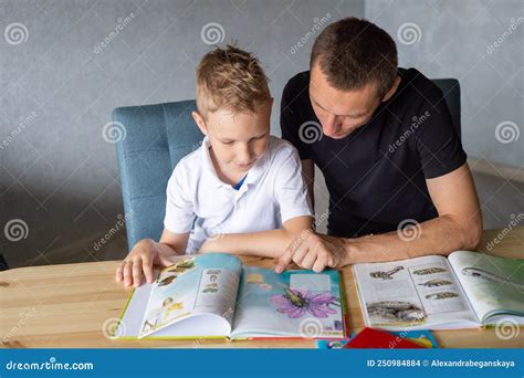 A Cute Boy is Sitting at the Table with His Dad and Watching a Book ...
