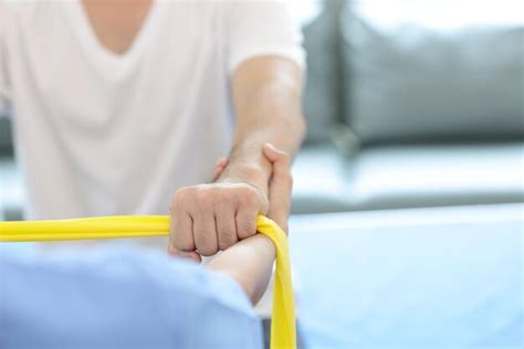 Nurse doing physiotherapy arm to male patient using elastic band in ...