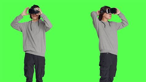Young adult enjoys virtual reality tech in studio with greenscreen backdrop, using interactive ...