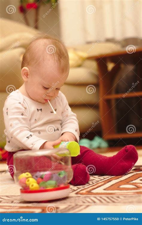 A Small Child is Sitting on the Floor in the Room and Playing with Ear ...