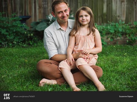 Little girl sitting on father's lap in backyard stock photo - OFFSET