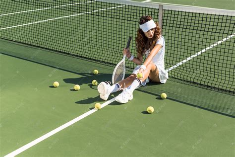 漂亮的女子网球运动员与球拍坐在网球网附近网球场周围球高清摄影大图-千库网