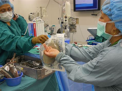 Operating Room Circulating RN using sterile technique to open supplies to a scrub. In the ...