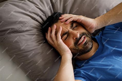 Premium Photo | Bearded young man waking up with a headache touching his head having a migraine ...