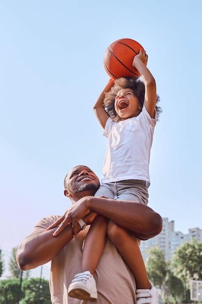 Happy african american father lifting his kid up and helping him score ...