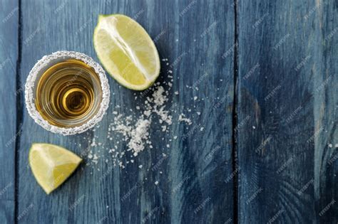 Tequila dorado en vidrio con sal y lima sobre un fondo azul de madera ...