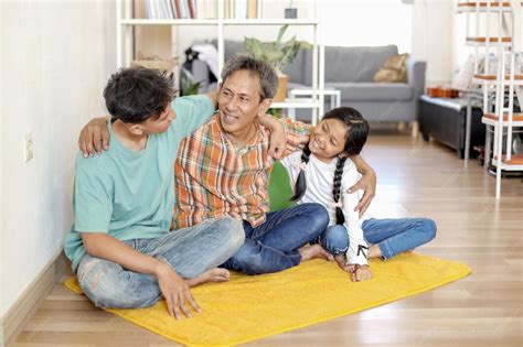 Cheerful asian family embracing father together while sitting on floor ...