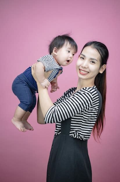Young mother lift up little baby, play and having fun on pink ...