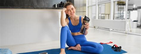 Portrait of smiling fitness instructor drinks water from bottle sits on ...