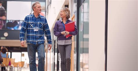 Two Mature Students Or Teachers Walking Through Communal Hall Of Busy ...