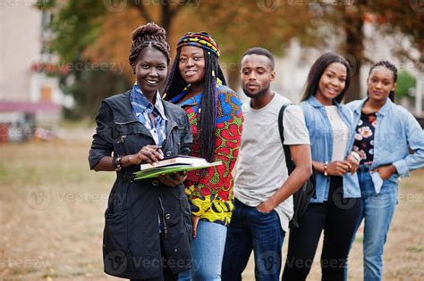 Row of group five african college students spending time together on campus at university yard ...