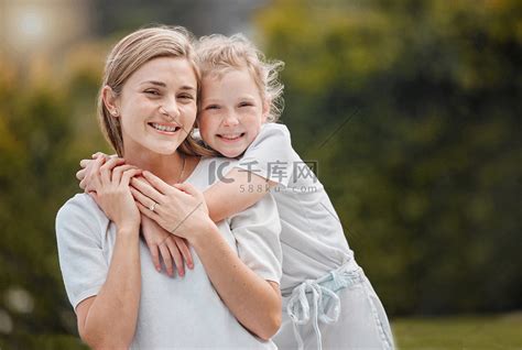 一个可爱的小女孩从后面拥抱她的母亲，同时在家里的花园里与她建立亲密关系的肖像。高清摄影大图-千库网