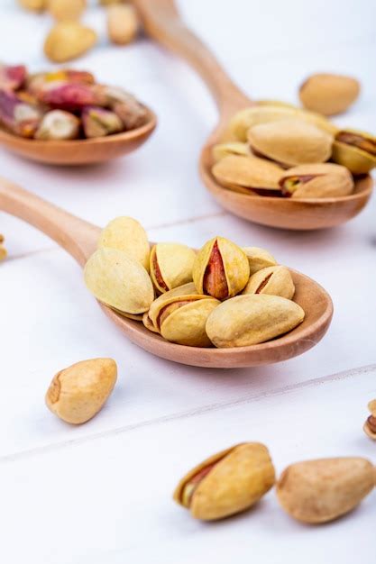 Side view of pistachio nuts on a wooden spoon on white background ...