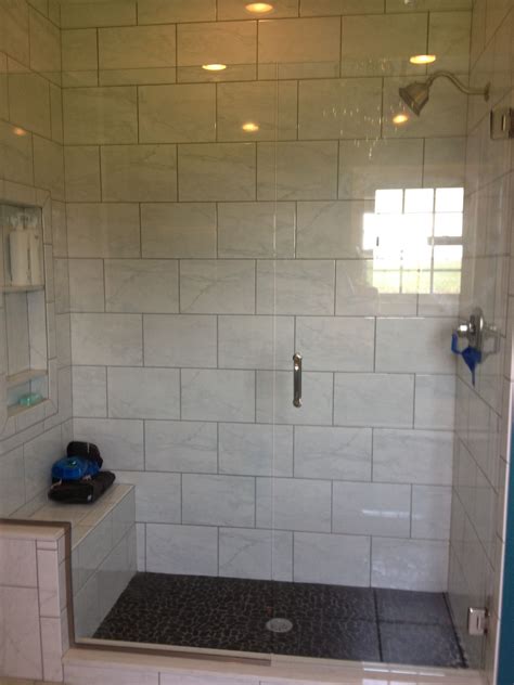 Glass shower with marble tiles and gray grout. Black pebble floors ...