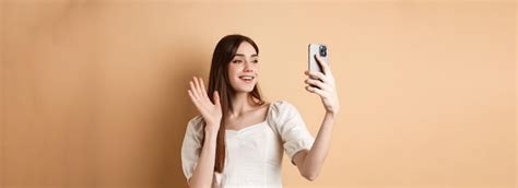 Dziewczyna na czacie wideo przez telefon machająca ręką przed kamerą ...