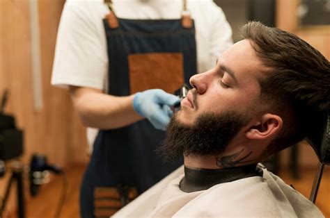 Jeune homme se faisant coiffer sa barbe chez le coiffeur | Photo Gratuite