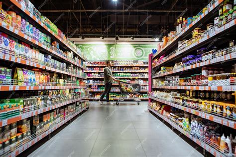 Young man with shopping cart between store shelf grocery | Premium Photo